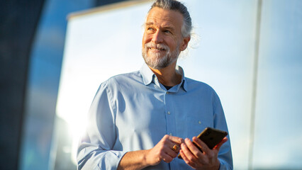 Senior man smiling and holding smartphone in urban setting