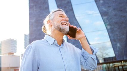 Elderly man laughing on phone in modern urban setting
