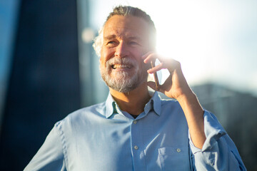 Happy senior man talking on phone in bright sunlight outdoors