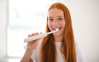 A cheerful woman happily enjoys her morning routine while brushing her teeth in a bright, sunny...