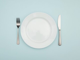Clean plate, fork and knife on light blue background