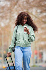African American woman traveling with suitcase and checking phone