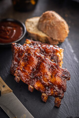 Pork BBQ glazed ribs and sauce on black table.