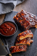 Pork BBQ glazed ribs and sauce on black table.