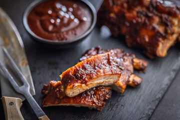 Pork BBQ glazed ribs and sauce on black table.