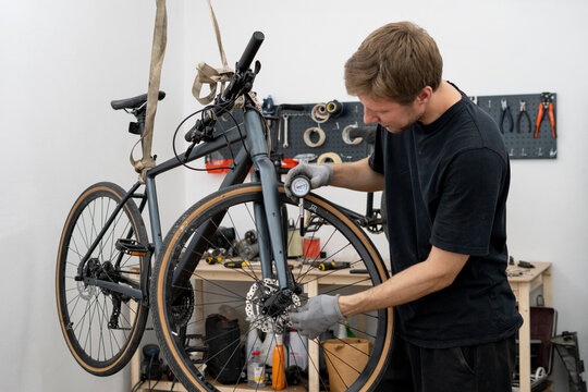 A person is adjusting the tire pressure of a bicycle using a hand-held gauge. The setting is a well-equipped bike shop