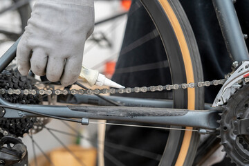 A cyclist applies lubricant to the bicycle chain while working on the bike in a workshop, ensuring...