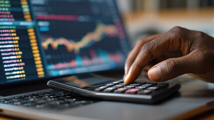 Person using calculator near laptop with stock charts