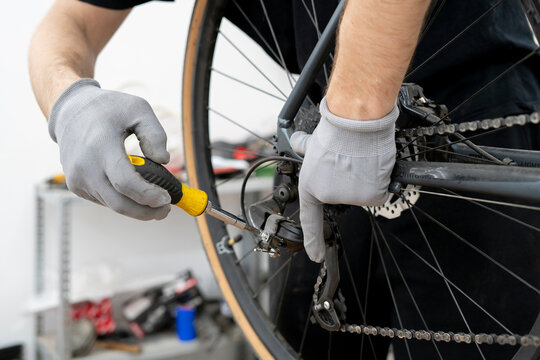 A mechanic is making adjustments to a bicycle tensioner using a screwdriver in a well-lit workshop