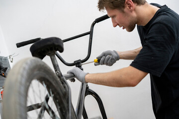 Obraz premium A person is carefully installing new bicycle handlebars in a workshop, using a screwdriver while wearing gloves. The bike rests on a stand for easy access.
