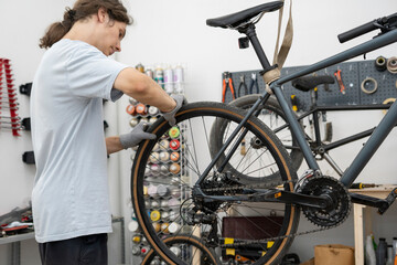 A bicycle mechanic repairs the rear wheel of a bike in a well-lit workshop, focusing on the brake...