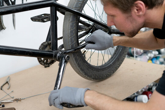 A cyclist is adjusting the seat of a BMX bike in a well-equipped workshop. Various tools and equipment are visible in the background, enhancing the repair process.