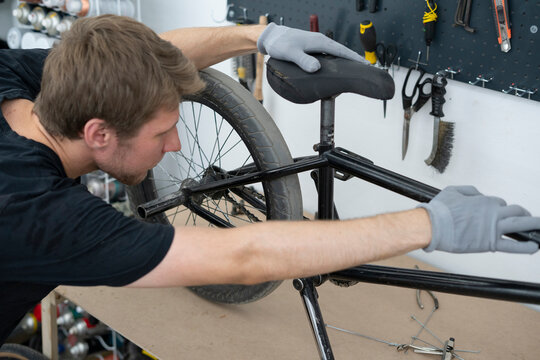 A cyclist is adjusting the seat of a BMX bike in a well-equipped workshop. Various tools and equipment are visible in the background, enhancing the repair process. - Powered by Adobe