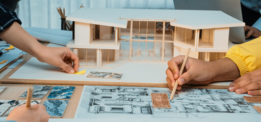 A collaborative workspace scene featuring hands engaged in creating architectural models and design...