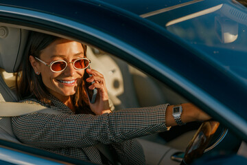 A fashionable and stylish woman confidently enjoys a phone call while driving her car along the city streets