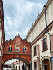 Obraz premium Red brick archway in a historic European street with pedestrians and buildings in Krakow, Poland.
