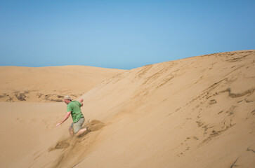An adult man sprints down steep golden dunes near Essaouira, kicking up thick sand clouds with each...