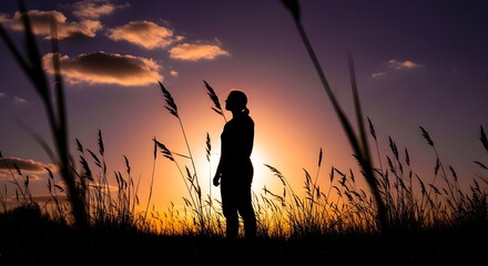 Silhouette of a woman standing in a grassy field at sunset, looking up at the colorful sky.