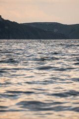 Obraz premium Tranquil scene of a bay with calm water and soft reflections during a nearly sunset sky, with hills visible in the background.