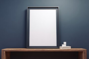 Blank black frame standing on wooden table against dark blue wall background.