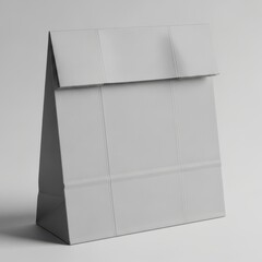 A simple gray paper lunch bag with a folded top stands upright isolated on a clean white background isolated on white background