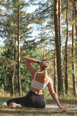 Mindful outdoor yoga in a pine forest: a woman stretches on a mat, breathes deeply, relaxes and...