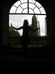 A silhouette of a girl dressed as a devil with horns stands against the backdrop of a large iron...