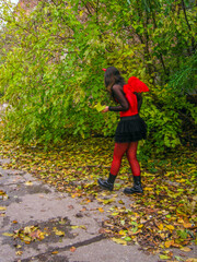 A girl dressed as a devil with horns collects autumn leaves	

