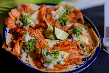 Mexican dish featuring tacos al pastor with pineapple, onion, cilantro, and lime slices served on corn tortillas, vibrant and flavorful.
