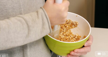 Stirring adult woman mixing rolled oats in home kitchen, with green bowl and spatula