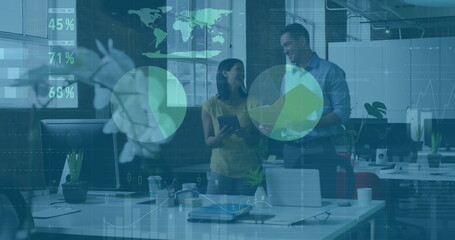 Discussing two coworkers reviewing reports and tablet at office desk, with floating data graphics