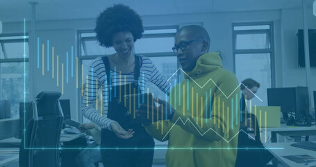 Reviewing printed report, co-workers in yellow hoodie and overalls leaning in office, with charts