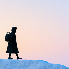 Person in black coat walks along rocky surface against pastel sky, evoking sense of solitude and contemplation