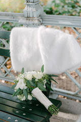 Elegant white fur stole draped over a park bench beside a fresh flower bouquet in autumn setting