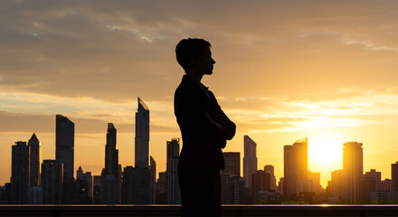 Confident businesswoman silhouetted against stunning sunset over city skyline, success concept