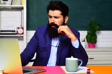 Pensive student preparing for exam or test at university. Learning, education. Thoughtful male student taking notes in laptop. Serious school teacher or businessman working with laptop at workplace.
