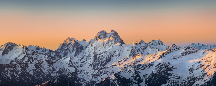 Panoramic view of the Ushba and Skhelda peaks at sunrise under the clolrful sky. Steep rocky caucasian mountains, a part of the Main Caucasian range, in winter sunny morning.