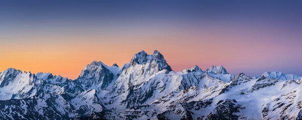 Panoramic view of the Ushba and Skhelda peaks at sunrise under the clolrful sky. Steep rocky...