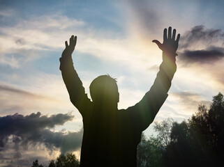 Silhouette of a person with raised arms against a dramatic sky with sun rays breaking through clouds