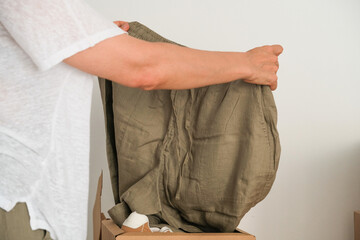 Woman holding linen pants in her hands while unpacking delivery box at home after online shopping....