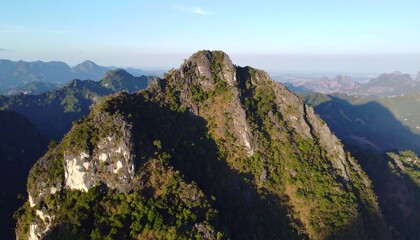 Fototapeta premium High-angle view of rugged mountain peaks and valleys, showcasing a tapestry of lush vegetation and dramatic rock formations under a clear sky.
