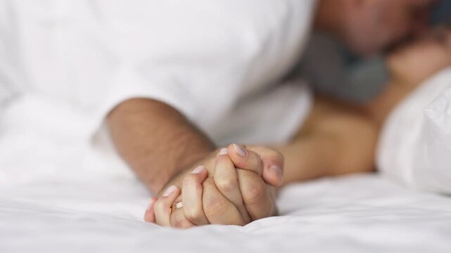 A sensual couple enjoys their intimacy in bed, holding hands. Concept Connection and affection in a private moment.