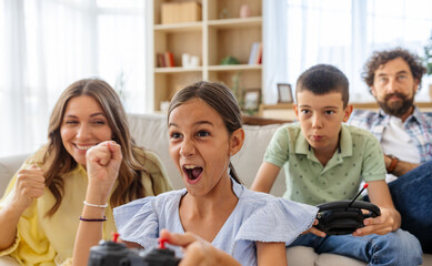 Little girl celebrating victory against brother in video game as parents watch
