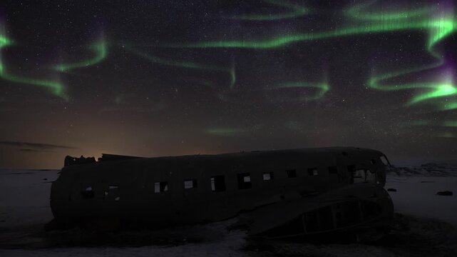 Time lapse of Aurora borealis above a crashed DC-3 Plane in Solheimasandur Iceland during winter. Tourism landmark at night with stars and sky.