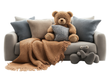 Teddy bear sits comfortably on a sofa surrounded by throw pillows and knitted blankets creating a cozy and relaxing atmosphere