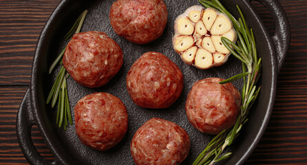 Raw meatballs seasoned with garlic and rosemary ready to be cooked in a cast iron pan, on a dark...