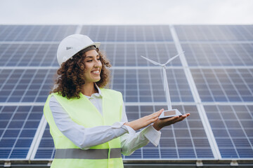 Female engineer holding small wind turbine model in front of solar panels