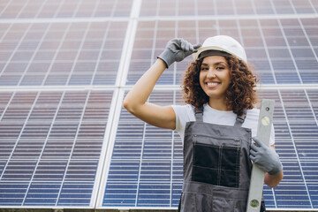 Female engineer working on solar panels installation, adjusting her helmet and smiling