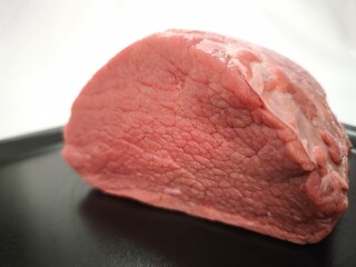 A piece of beef meat on a black plate in close-up. Raw meat