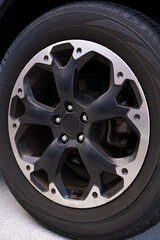 Detailed close-up of black and silver alloy wheel rim with tire on red vehicle. Concept for automotive repair, maintenance, driving, and transportation.